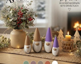May include: Four cone-shaped gnome figurines with rounded noses, two in tan and two in purple, arranged next to a beige vase filled with greenery and red berries, a honeycomb candle in a woven holder, and wooden tree cutouts.