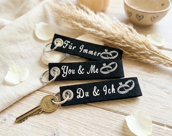May include: Three rectangular black felt keychains with silver metal grommets and rings. Each features white text and a glittery silver ring graphic. The text reads "Für Immer", "You & Me", and "Du & Ich". One keychain has a brass Yale key attached.