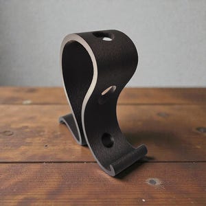 May include: A matte black wall hook with a curved, S-shaped profile. The hook features a textured exterior surface and a smooth, light-colored interior edge. It includes two circular mounting holes positioned vertically along the main body.