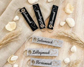 May include: Six rectangular keychains with metal rings. Three are black with white text reading Seelenmensch, Lieblingsmensch, and Herzensmensch, each with a heart icon. Three are light gray felt with black text and heart outlines.