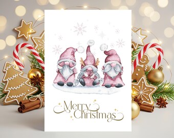 May include: A white greeting card featuring a watercolor illustration of three gnomes wearing pink hats and white beards, standing on a snowy base with snowflakes above. The text Merry Christmas is printed in gold cursive at the bottom of the card.
