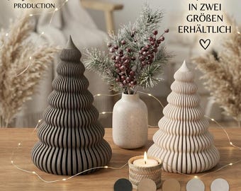 Può includere: Due alberi decorativi a forma di cono a coste in grigio scuro e crema, posizionati accanto a un vaso in ceramica maculata con rami di pino ghiacciati con bacche rosse e una piccola candela in un supporto intrecciato.