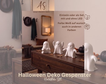May include: Four white ghost figurines with smooth surfaces and rounded features, displayed on a dark wooden surface. The ghosts are arranged in a row, with some positioned near small dark pumpkins and scattered dried autumn leaves.