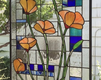 May include: Stained glass panel featuring orange poppy flowers with green stems and leaves. The background includes blue, green, and clear glass sections, all framed in black. A decorative floral art piece.