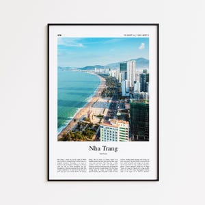 Op de afbeelding: Een ingelijste print met een kustgezicht van Nha Trang, Vietnam. De afbeelding toont een strand, turquoise water en een stadsgezicht met hoge gebouwen. De print bevat de naam van de stad en geografische coördinaten.
