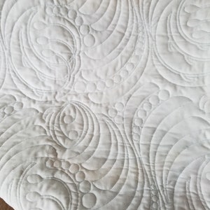 May include: White quilted fabric with a repeating pattern of curved lines and circles. The quilting is done in a light gray thread.
