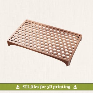 May include: A rectangular copper-colored tray featuring a repeating hexagonal honeycomb pattern across its surface. The tray has a raised edge and small feet at each corner, providing a slightly elevated platform with a grid-like structure.
