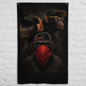 Peut inclure: Une tapisserie murale verticale représentant trois chimpanzés sur un fond sombre. L'un porte un casque orange et une casquette noire, un autre des lunettes à monture jaune et une casquette noire, et le troisième un bandana rouge et une casquette noire.