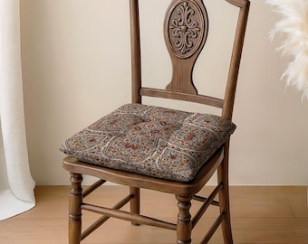 May include: A wooden chair with a high back featuring a carved oval medallion at the center. The seat is covered by a square cushion displaying a dense, multi-colored floral and paisley pattern in shades of red, blue, gold, and cream.