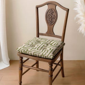 May include: A wooden chair with a decorative back and a square cushion. The cushion features a beige background with a green geometric pattern. The chair is made of dark wood and has a classic design, suitable for home decor.