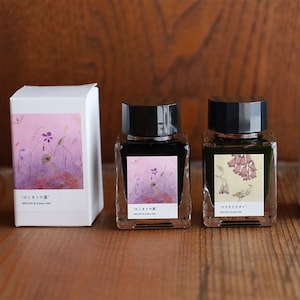 May include: Two glass ink bottles with black lids and matching boxes. The bottles have labels with floral designs and Japanese text. The boxes feature similar artwork. The ink appears to be dark in colour.