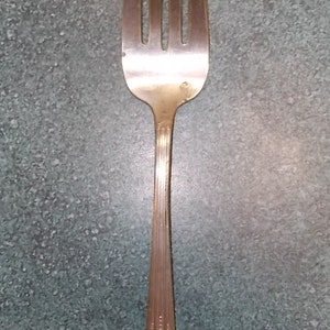 May include: A silver fork with a decorative pattern on the handle. The fork has four tines and is in good condition.