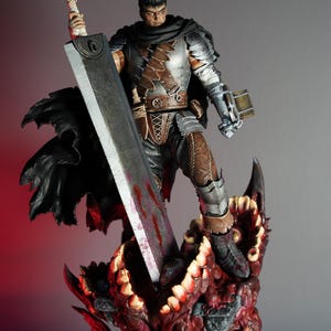 Könnte beinhalten: Detaillierte Figur eines Kriegers in silberner Rüstung, der ein großes, blutbeflecktes Schwert hält. Die Figur steht auf einem roten, monströsen Sockel mit scharfen Zähnen. Der Krieger hat einen schwarzen Umhang und einen entschlossenen Gesichtsausdruck.