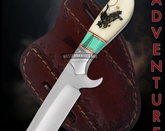 Peut inclure: Couteau artisanal avec un manche en os représentant un cow-boy sur un taureau, des accents turquoise et une lame en acier inoxydable. Comprend un étui en cuir marron. Le mot "ADVENTURE" est imprimé.