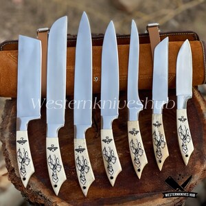 May include: A set of seven stainless steel knives with cream-colored handles featuring a black decorative design. The knives are displayed on a wooden surface with a brown leather carrying case in the background. The text "WesternKniveshub" is visible.
