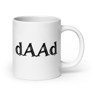 Op de afbeelding: Witte keramische mok met de zwarte tekst "dAAd" in handschriftstijl. De mok heeft een gebogen handvat en een glanzende afwerking. Een eenvoudig, modern ontwerp, ideaal voor koffie of thee.