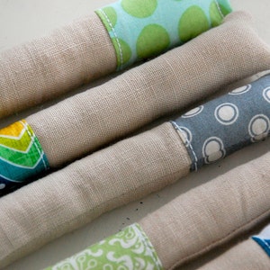 Może przedstawiać: Cztery ręcznie robione zabawki dla kot&oacute;w z kocimiętką, z r&oacute;żnymi wzorzystymi pokrowcami z tkaniny. Zabawki są wykonane z naturalnego lnu i wypełnione kocimiętką. Wzory obejmują zielone i niebieskie kształty geometryczne, niebieskie i białe kropki oraz zielone i ż&oacute;łte kształty geometryczne.