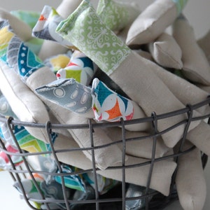 Może przedstawiać: Kosz druciany wypełniony ręcznie robionymi poduszkami pokrytymi tkaniną. Poduszki są w r&oacute;żnych kolorach i wzorach, w tym zielonym, niebieskim, pomarańczowym i białym.