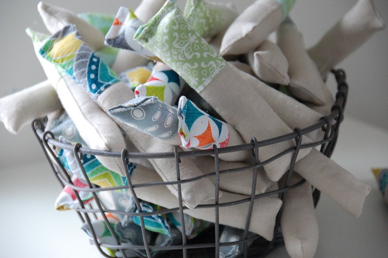 Może przedstawiać: Kosz druciany wypełniony ręcznie robionymi poduszkami pokrytymi tkaniną. Poduszki są w r&oacute;żnych kolorach i wzorach, w tym zielonym, niebieskim, pomarańczowym i białym.