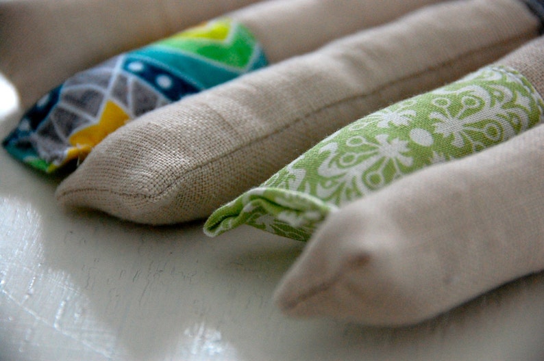 Może przedstawiać: Cztery poduszki do oczu pokryte tkaniną w r&oacute;żnych wzorach. Poduszki są beżowe z r&oacute;żnymi kolorowymi wzorami z przodu. Wzory obejmują zielono-białe kwiaty, niebiesko-białe wzory geometryczne i ż&oacute;łto-zielone wzory geometryczne.