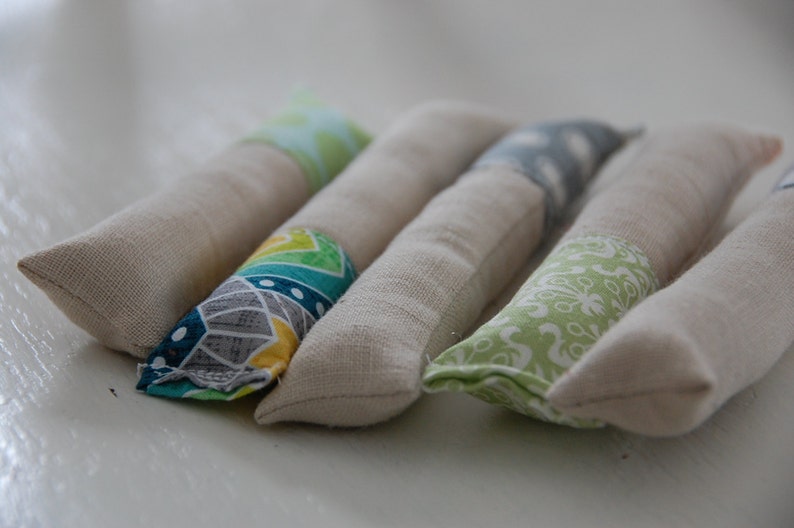 Może przedstawiać: Pięć ręcznie robionych zabawek z kocimiętką wykonanych z naturalnego materiału z r&oacute;żnymi kolorowymi wzorami. Zabawki mają kształt długich cylindr&oacute;w i są wypełnione kocimiętką.