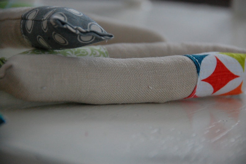 Może przedstawiać: Rurka z beżowego materiału z kolorowym geometrycznym wzorem na jednym końcu. Wz&oacute;r przedstawia białą gwiazdę z czerwonymi, pomarańczowymi, ż&oacute;łtymi, zielonymi i niebieskimi akcentami.