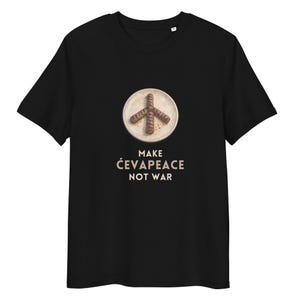 May include: Black t-shirt featuring a peace sign made of grilled sausages on a plate. The text "MAKE ĆEVAPEACE NOT WAR" is printed below the image. The shirt is made of a soft material.