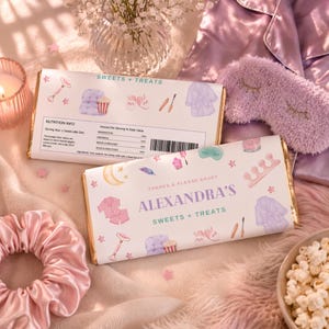 May include: Two chocolate bars with gold foil edges are displayed. The wrappers feature illustrations of pajamas, spa items, and the text "SWEETS + TREATS" and "ALEXANDRA'S SWEETS + TREATS". A pink scrunchie, eye mask, and popcorn are also visible.