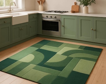 May include: A green geometric patterned rug in a kitchen setting. The rug features various shades of green in a modern design. The kitchen has green cabinets, a stainless steel oven, and a white sink. The rug is rectangular and covers a portion of the wooden floor.