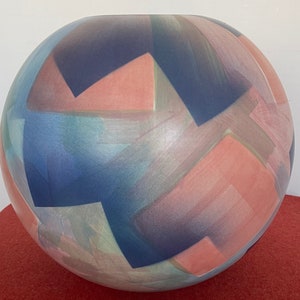 May include: A round ceramic vase with a geometric pattern in shades of blue, pink, and green.