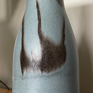 May include: A light blue ceramic vase with a brown glaze design. The vase has a rounded body and a narrow neck.