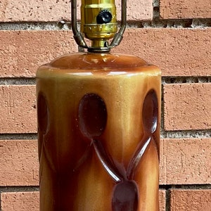 May include: A brown and tan ceramic table lamp with a quilted design. The lamp has a metal shade and a black base.