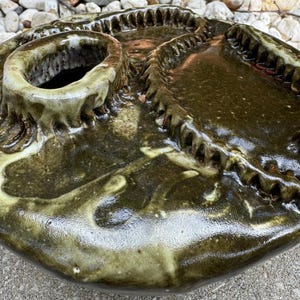 May include: A ceramic vase with a green and white glaze. The vase has a unique, textured design with a raised rim and a small opening at the top.