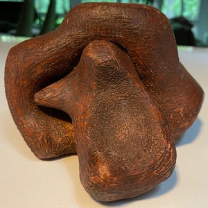 May include: Abstract ceramic sculpture with a textured, reddish-brown finish. The sculpture is composed of multiple rounded forms that interlock.