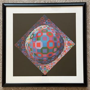 Puede incluir: Una impresi&oacute;n enmarcada de un dise&ntilde;o geom&eacute;trico abstracto colorido. El dise&ntilde;o presenta una esfera compuesta por cuadrados y rect&aacute;ngulos en tonos de rojo, azul, verde y morado. La esfera se coloca sobre un fondo marr&oacute;n oscuro.