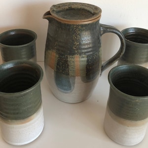 May include: Set of five ceramic mugs and a pitcher with a green, brown, and white glaze. The mugs and pitcher have a rustic, handmade look.
