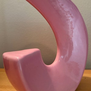 May include: A pink ceramic sculpture in the shape of a crescent moon. The sculpture is smooth and glossy.