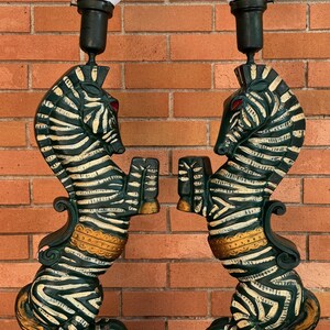 K&ouml;nnte beinhalten: Paar dekorativer Tischlampen mit zebraf&ouml;rmigen Sockeln, schwarz-wei&szlig;en Streifen und roten Augen. Die Lampen haben wei&szlig;e, konisch geformte Schirme und sind in Gr&uuml;n, Gold und Schwarz lackiert. Die Lampen sind etwa 76 cm hoch.