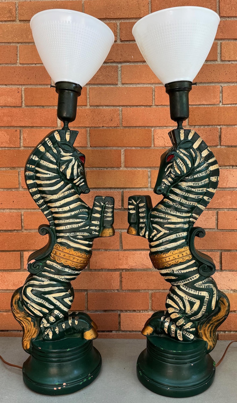 K&ouml;nnte beinhalten: Paar dekorativer Tischlampen mit zebraf&ouml;rmigen Sockeln, schwarz-wei&szlig;en Streifen und roten Augen. Die Lampen haben wei&szlig;e, konisch geformte Schirme und sind in Gr&uuml;n, Gold und Schwarz lackiert. Die Lampen sind etwa 76 cm hoch.