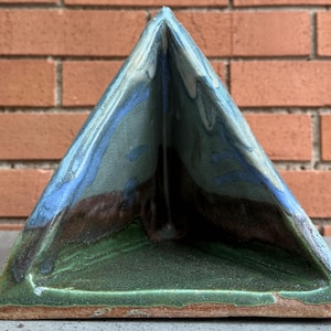 May include: A triangular ceramic planter with a green, blue, and brown glaze. The planter has a wide opening at the top and a narrow base.
