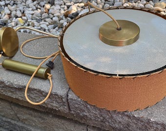 May include: Vintage mid-century modern pendant light with a woven brown shade, a perforated silver metal top, and brass accents. Includes a cylindrical brass component and a round brass ceiling mount. The light fixture is designed for overhead illumination.