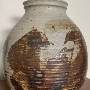 May include: A ceramic lidded jar with a white glaze and brown and tan abstract designs. The jar has a round body and a small, round lid.