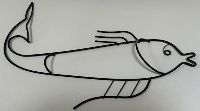 May include: Black metal fish wall decor with a stylized design. The fish has a curved body, a long tail, and a detailed head with a small eye.