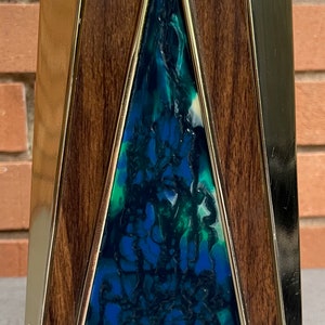 May include: A triangular shaped decorative object with a wood frame and a blue, green, and white resin inlay.
