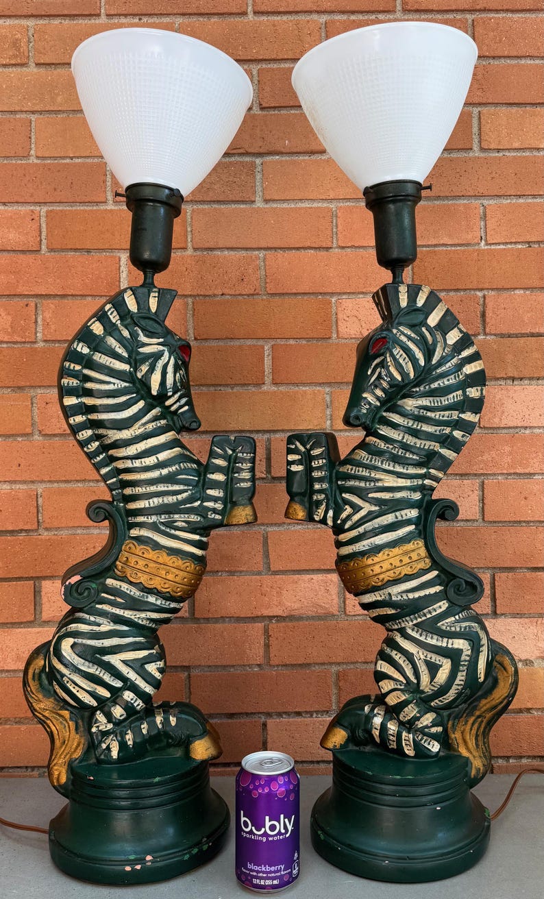 K&ouml;nnte beinhalten: Paar Vintage-Tischlampen mit zebraf&ouml;rmigen Sockeln. Die Lampen haben wei&szlig;-schwarze Zebrastreifen, rote Augen und goldfarbene Akzente. Jede Lampe hat einen wei&szlig;en, konisch geformten Schirm. Die Lampen stehen auf einem gr&uuml;nen Sockel.