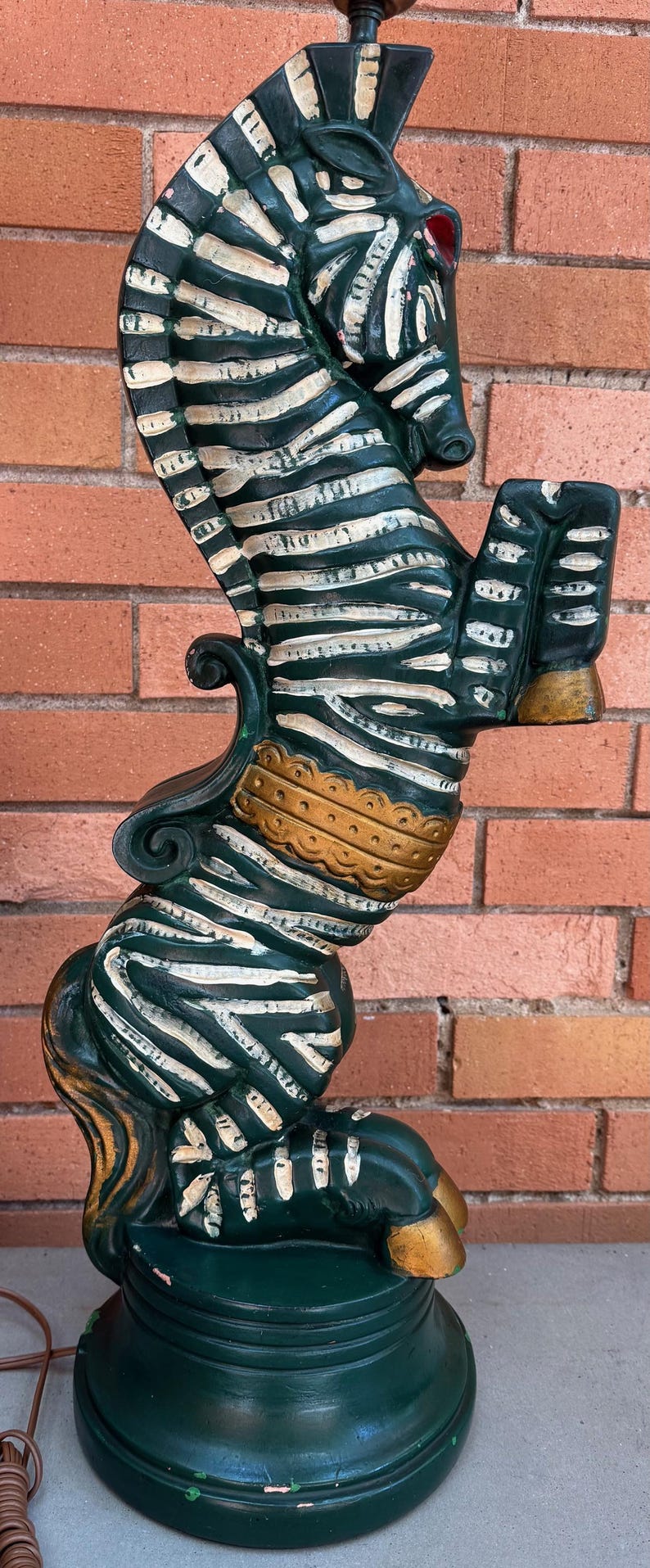 K&ouml;nnte beinhalten: Vintage Seepferdchen-Lampe mit dunkelgr&uuml;nem Sockel und K&ouml;rper, wei&szlig;en Streifen und goldenen Akzenten. Die Lampe hat die Form eines Seepferdchens mit einem zebraartigen Muster und einem roten Auge.