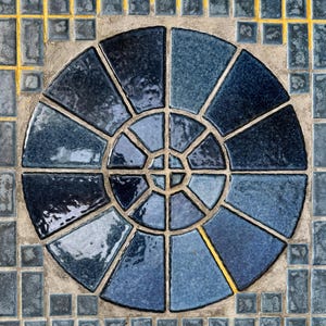 May include: A circular mosaic tile design featuring a central sunburst pattern in shades of blue. The mosaic is surrounded by a border of smaller blue tiles with gold accents. The design is suitable for home decor.