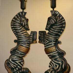 K&ouml;nnte beinhalten: Paar dekorative Tischlampen mit zebraf&ouml;rmigen Sockeln mit schwarz-wei&szlig;en Streifen, goldenen Akzenten und wei&szlig;en Glasschirmen. Die Lampen haben einen dunkelgr&uuml;nen Sockel und sind so gestaltet, dass sie sich gegen&uuml;berstehenden Zebras &auml;hneln.