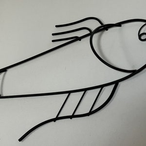 May include: Black metal fish wall decor with a stylized design. The fish has a curved body and a large, open mouth.