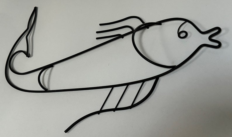 May include: Black metal fish wall decor with a stylized design. The fish has a curved body and a large, open mouth.